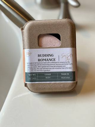 Budding Romance Sea Salt and Clay Spa Soap Bar packaged in kraft paper, shown on a bathroom counter